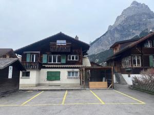a building in a parking lot in front of a mountain at Alpina Appartment Kandersteg in Kandersteg