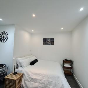 a white bedroom with a bed and a clock on the wall at Maple House - Inviting 1-Bed Apartment in London in London