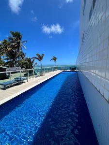 a swimming pool with the ocean in the background at Apartamentos Pe na areia no Caribessa in Tambaú