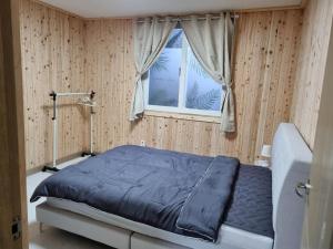 ein Schlafzimmer mit einem Bett mit blauer Decke und einem Fenster in der Unterkunft Amy House in Jeju-do