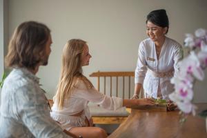 Dos mujeres están sentadas alrededor de una mesa con una mujer de pie en Teratai Villa Canggu by Ini Vie Hospitality en Canggu