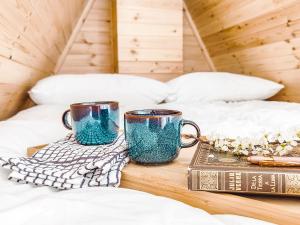 two coffee mugs and a book on a bed at Bective Mill Glamping & Camping 