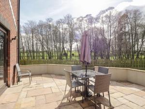 eine Terrasse mit einem Tisch, Stühlen und einem Sonnenschirm in der Unterkunft Mill End in Penrith
