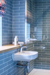 a blue tiled bathroom with a sink and a mirror at The Carpenters Arms in Great Wilbraham