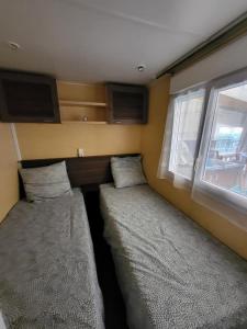Habitación pequeña con 2 camas y ventana en Mobil home 6 personnes Forêt des landes, en Mimizan