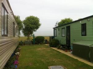 een groen huis met een tuin naast een huis bij Dymchurch Caravan Park on Romney Marsh in Dymchurch