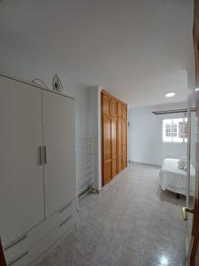 a white bedroom with a bed and a wooden cabinet at Apartamentos Las Canteras Arena in Las Palmas de Gran Canaria