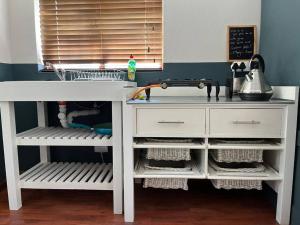 a kitchen counter with a white table and shelves at Pinchushion Cottage Fish Hoek in Fish hoek