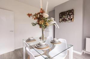 a dining room with a glass table with a vase of flowers at Luxury 3 bedroomed home in Kettering