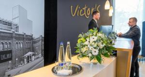 deux hommes debout sur un bureau avec un vase de fleurs dans l'établissement Victor's Residenz-Hotel Berlin Tegel, à Berlin