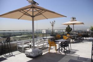 un patio con mesas, sillas y una sombrilla en Golden Tulip Opera Alger en Ouled Fayet