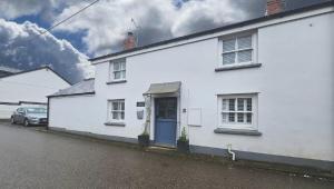 une maison blanche avec une porte bleue dans une rue dans l'établissement Church Cottage - Quaint farmhouse cottage with modern twist, Dog Friendly, Sleeps 6-7, à West Down