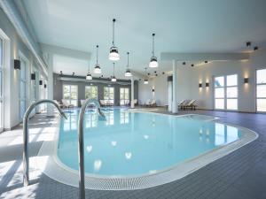 a large pool with blue water in a building at Reetland am Meer - Luxus Reetdachvilla mit 3 Schlafzimmern, Sauna und Kamin E27 in Dranske