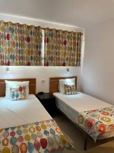 Habitación de hotel con 2 camas y cortinas con flores en Puskas Apartman, en Costa de Antigua