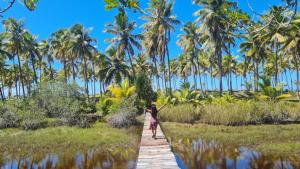 een vrouw die over een houten brug loopt voor palmbomen bij Nova Gaia Algodões in Marau
