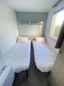 two beds in a small room with a window at - Mobilhome Camping Les Charmettes - Fun pass non inclus - in Les Mathes