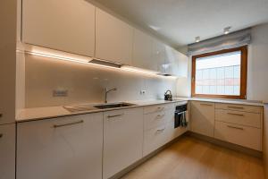 eine Küche mit weißen Schränken, einem Fenster und einem Waschbecken in der Unterkunft Casa al Parco Deluxe in Canazei