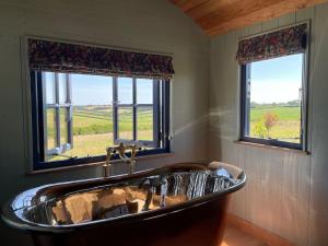 a bath tub in a bathroom with two windows at Novelist Shepherd's hut in Beaminster