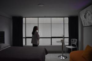 a woman standing in a bedroom looking out the window at Hotel Demetria in Huánuco