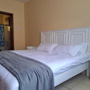 Elle comprend un grand lit blanc avec des draps et des oreillers blancs. dans l'établissement Shiks Apartment retreat, à Nairobi