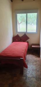uma cama vermelha num quarto com uma janela em La Soñada de La Majadita em San Agustín de Valle Fértil