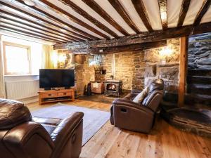 a living room with leather furniture and a stone fireplace at Cwm Yr Afon Mawr in Llanbedr