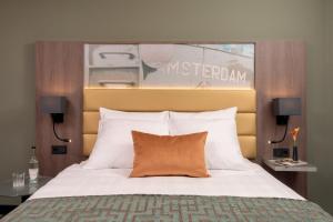 a bedroom with a large bed with an orange pillow at Leonardo Royal Hotel Amsterdam in Amsterdam