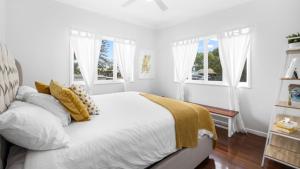 a white bedroom with a large bed with yellow pillows at The Blue Beachside Bungalow in Woorim +7 photos