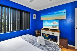 ein blaues Schlafzimmer mit einem Bett und einem TV an der Wand in der Unterkunft Sandhurst 5 in The Entrance