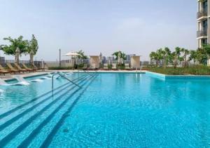 a large blue swimming pool with chairs and a building at Host and Stay - Collective tower 1, Dubai Hills Estate in Dubai