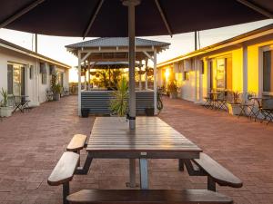 a wooden picnic table with an umbrella on a patio at API Pelican Beach Front Apartments Kalbarri in Kalbarri
