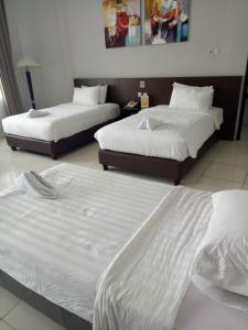 two beds in a hotel room with white sheets at Hotel Sindha in Ruteng
