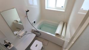La salle de bains blanche est pourvue d'une baignoire et d'un miroir. dans l'établissement Oak Village, à Hakuba