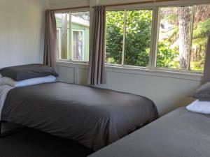 a bedroom with two beds and two windows at Cox Bay Cottage in Raglan