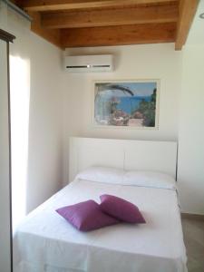 a white bed with a purple pillow on it at Pozzo Lazzaro Apartments in Santa Teresa di Riva