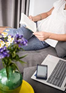 a woman sitting on a couch reading a book and a laptop at River View Boutique Apts in Ayia Napa