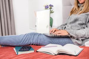 a woman sitting on a bed with a laptop and books at River View Boutique Apts in Ayia Napa