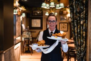 a man holding two plates of food in a restaurant at The Swan at Grasmere- The Inn Collection Group in Grasmere