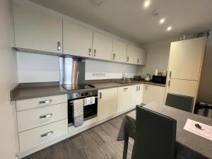 cocina con armarios blancos, mesa y nevera en Balcony Marina Apartment With City Skyline Views en Mánchester