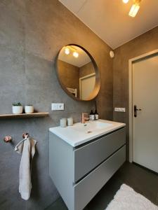 een badkamer met een witte wastafel en een spiegel bij Bohemian Wellness met hottub & sauna in Ewijk