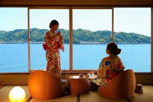 Dos mujeres en kimonos sentadas en sillas mirando hacia el agua en Ooedo Onsen Monogatari Nanki Kushimoto, en Kushimoto