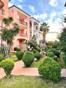 un bâtiment rose avec des arbres et des buissons devant lui dans l'établissement Casa vacanze Valledoria Q8732, à Valledoria