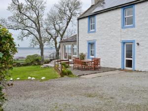 a white house with a table and chairs outside at Kirkbride Farmhouse - 28471 in Creetown