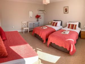 a bedroom with two beds with red blankets and a table at Kirkbride Farmhouse - 28471 in Creetown