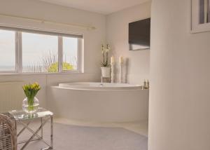 a white bathroom with a tub and a window at Boskerris Hotel in St Ives +42 photos