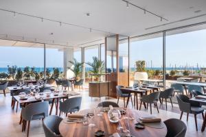 Hotel Marina Badalona في بادالونا: مطعم بطاولات وكراسي ونوافذ كبيرة