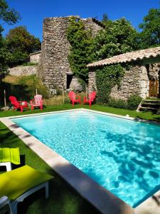 a swimming pool with red chairs and a stone house at Les MIMOSAS Gîte du Mas Haut in Saint-Jean-du-Gard