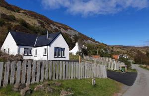 a white house with a fence next to a road at Bay View Bungalow in Uig