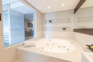 a white bathroom with a tub and a window at Delupo Apart Hotel in Criciúma