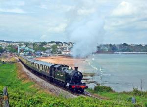 a steam train traveling down the tracks near the water at Hoburne Devon Bay stunning 3 bed luxury lodge in Paignton